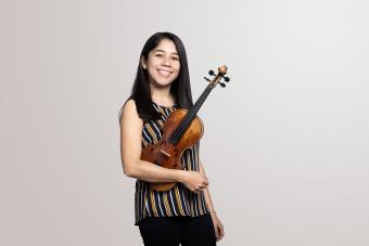 a violinist holds her instrument and smiles into camera