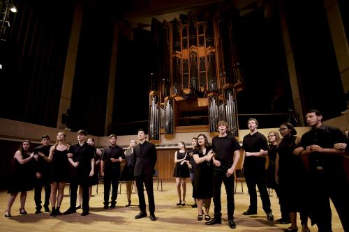 undergraduate opera students perform an opera scene on stage, dressed in black.