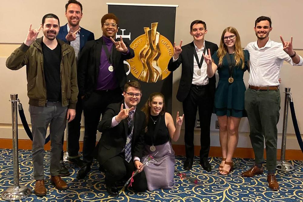 Members of zed standing giving the hook em sign