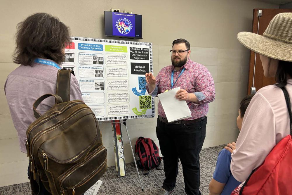 Michael Lenahan stands in front of a music education poster with several people watching him