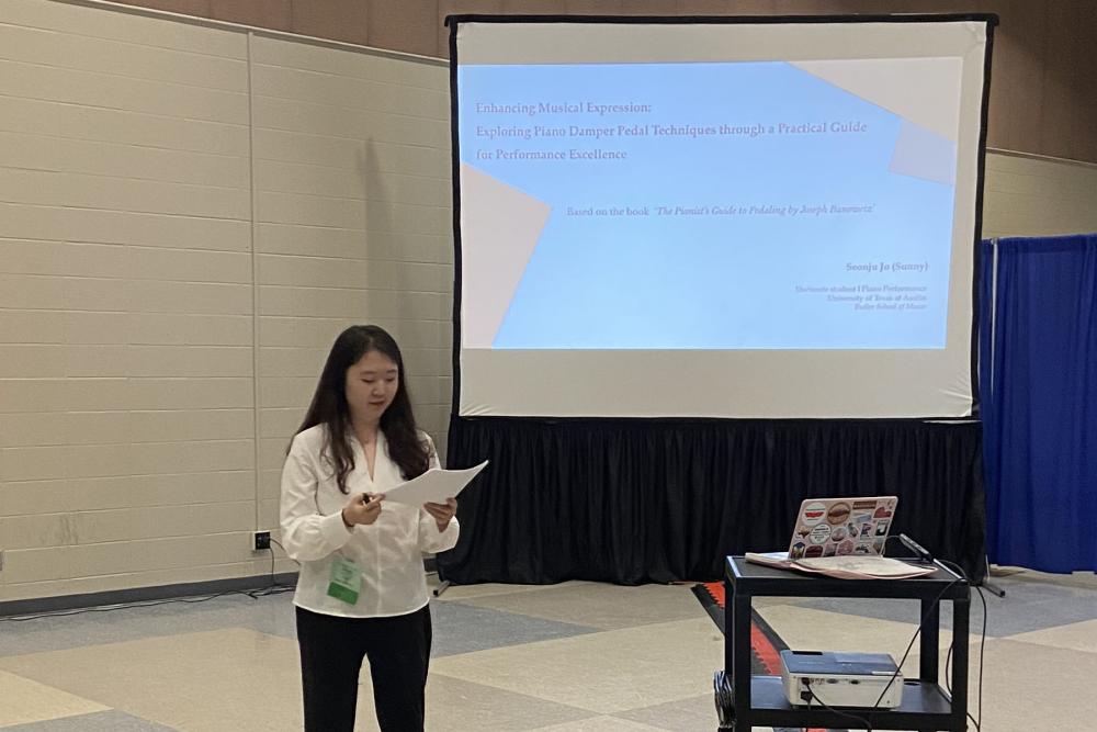 Student presents at a conference with a powerpoint screen behind them