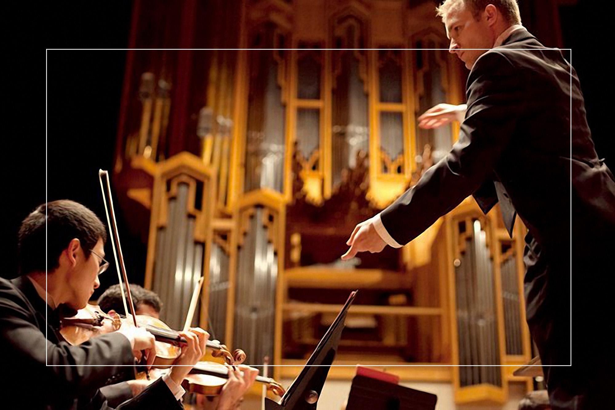 A conductor conducts a violin section in Bates Recital Hall