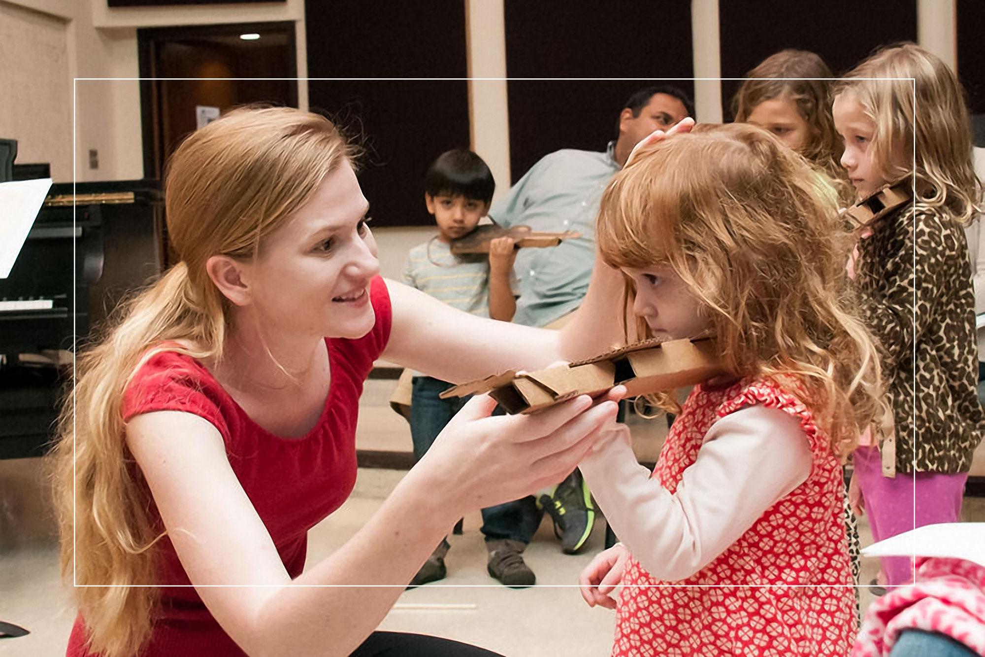 A student teacher assists a young violinist with playing position during a lesson.