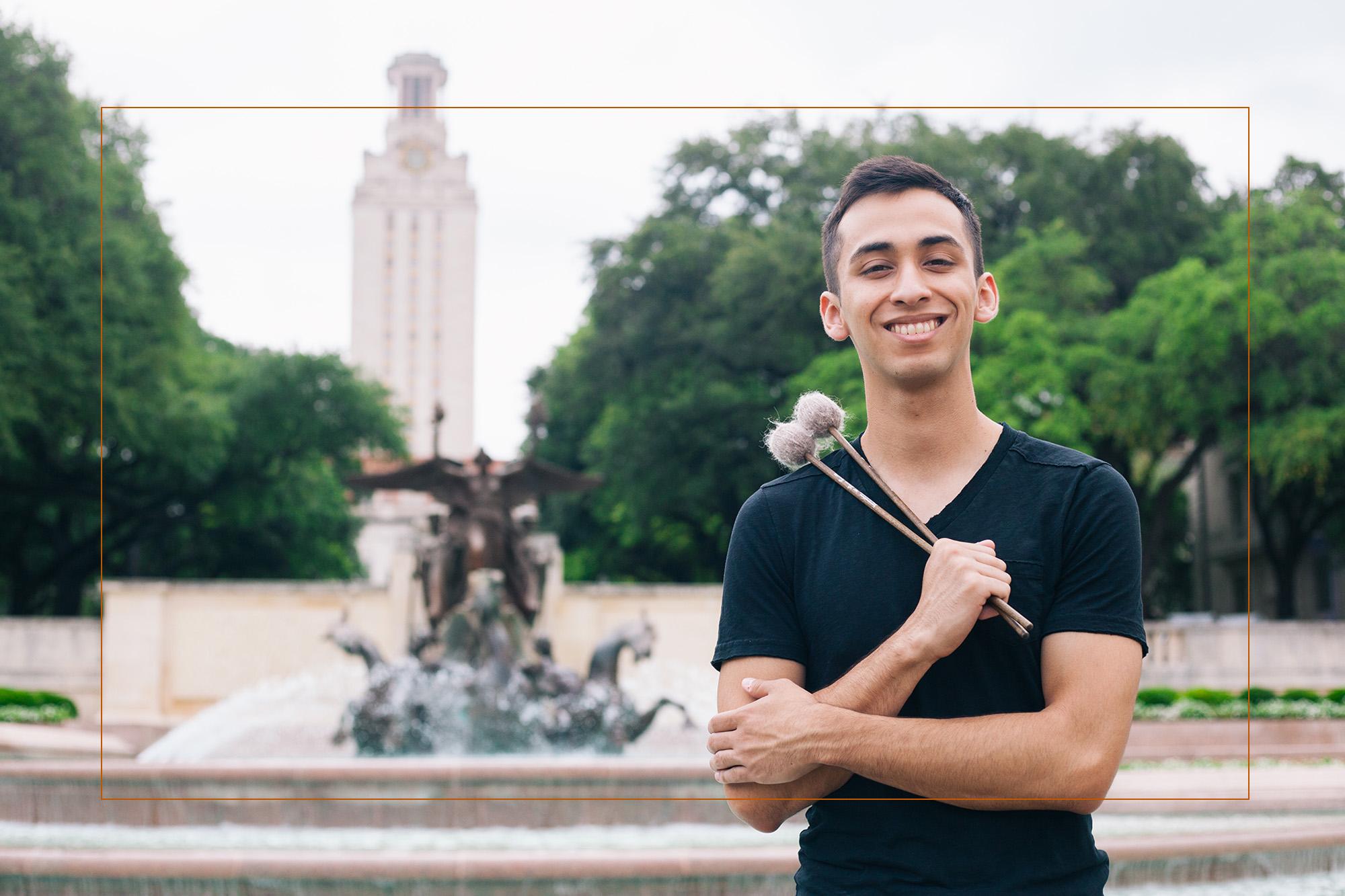 Male student with percussion mallets smiles at camera in front of the UT tower.