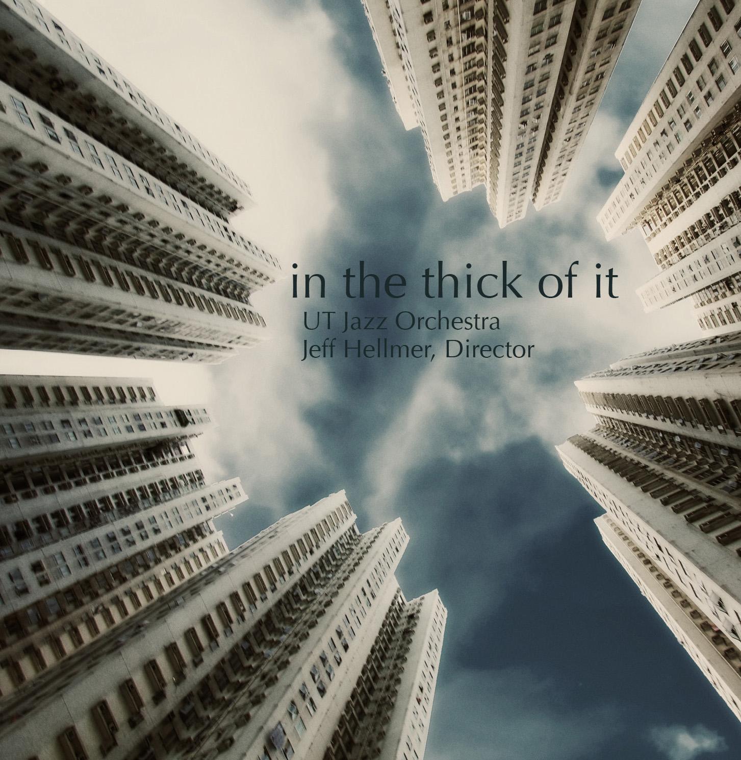 Recording Cover of "In the Thick of It"; High-rise buildings tower over the viewer on all sides with cloudy blue skies beyond.