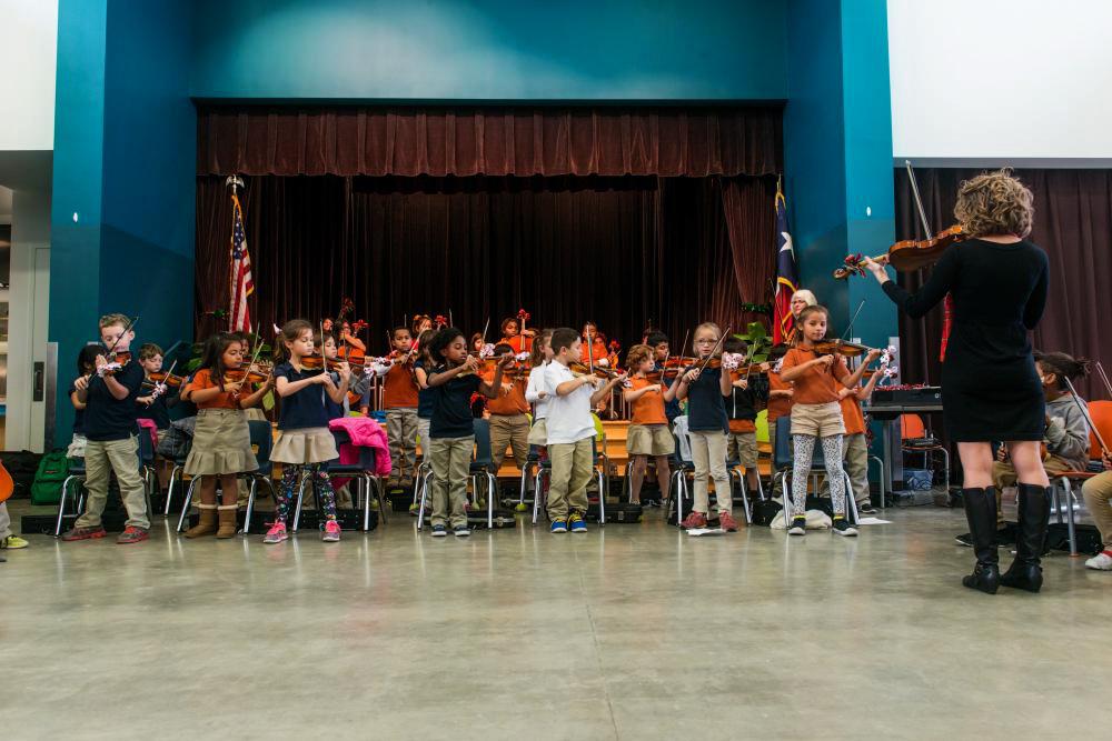 A group of young violinists receive instruction from a Butler student in the elementary school auditorium.