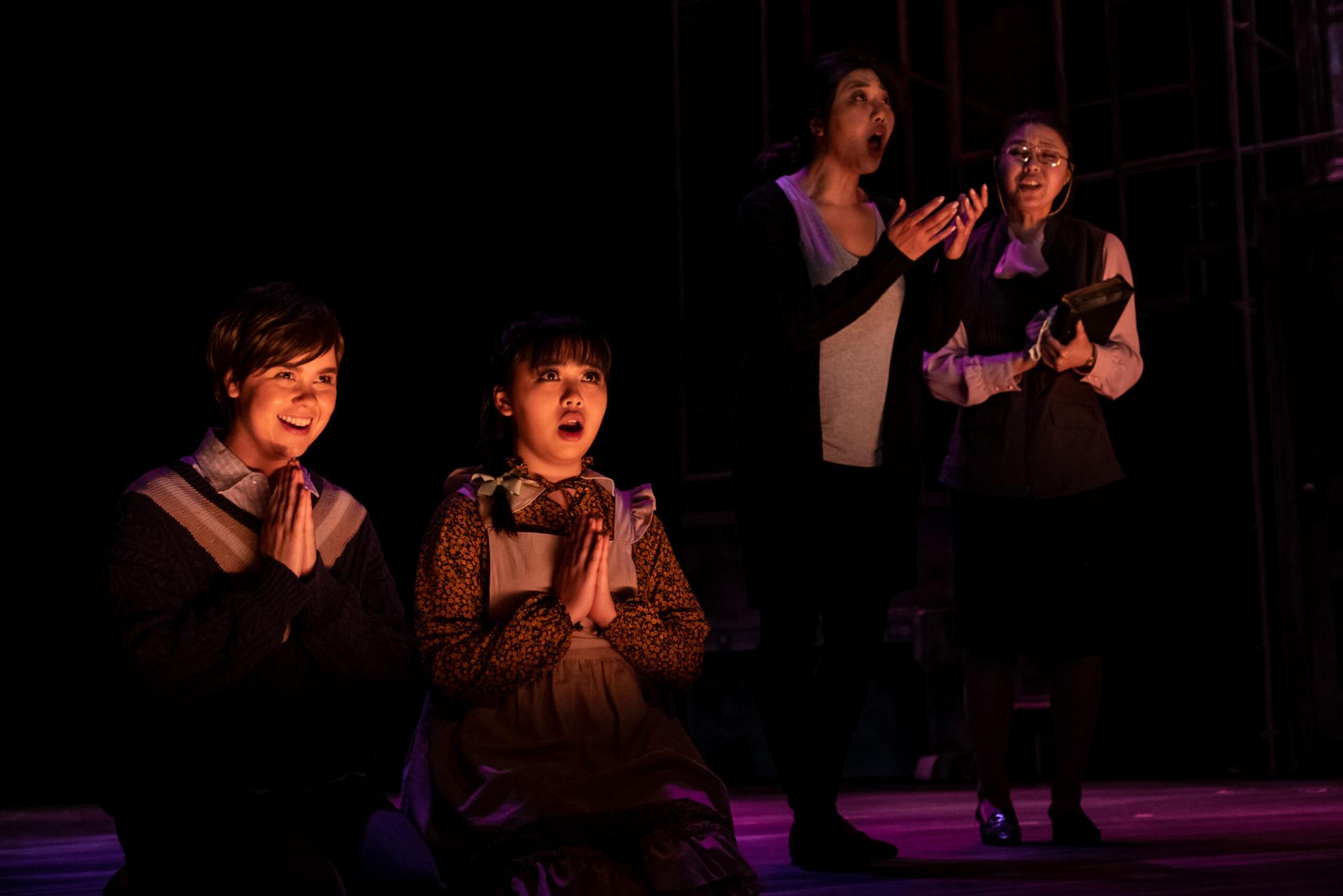 Two Children kneel and pray with cunning smirks while adults fret in the background