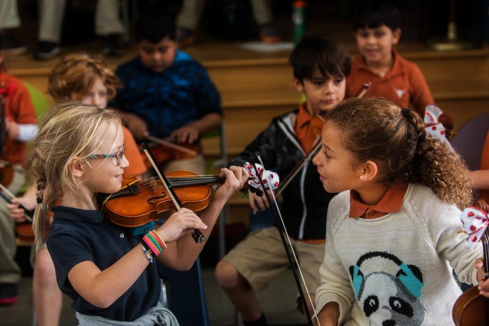 Two young violinists laugh happily during a group lesson.