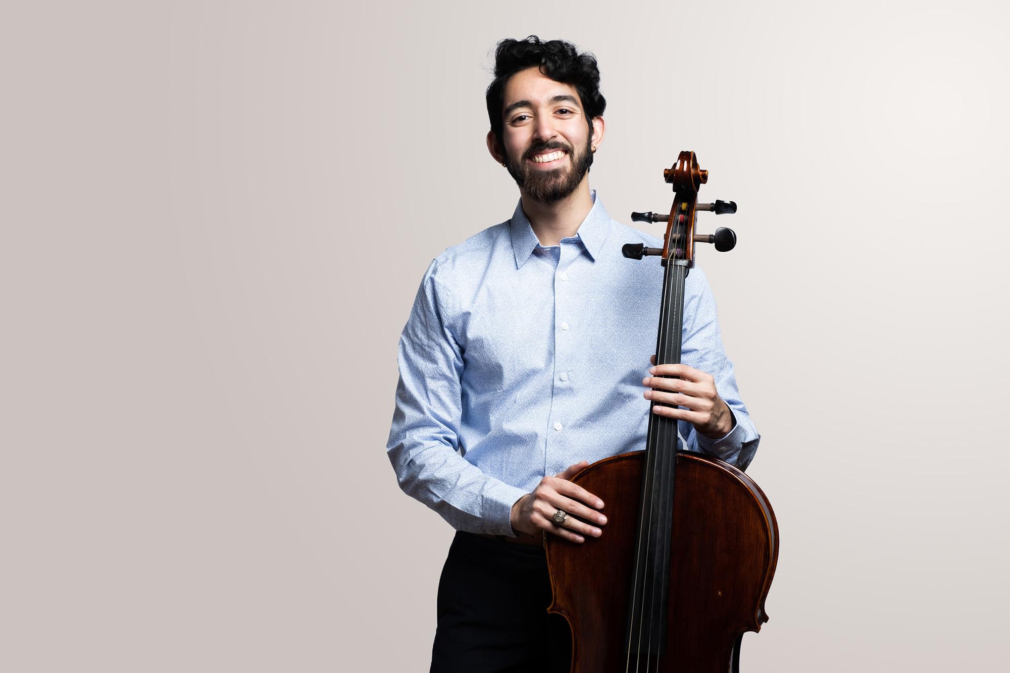 A Male cellist holds his instrument and smiles 