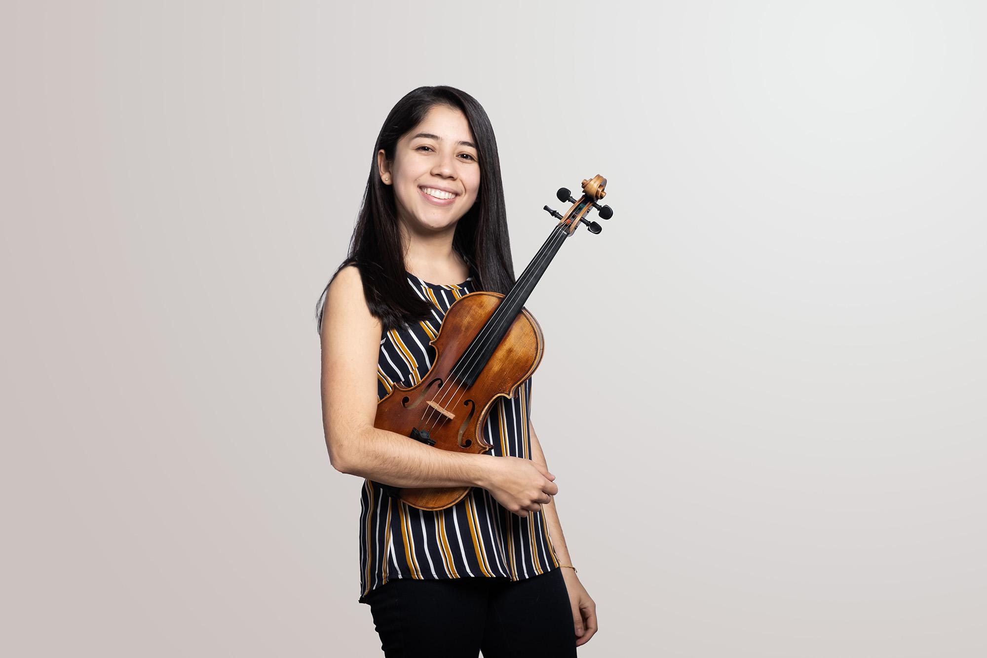 a violinist holds her instrument and smiles into camera