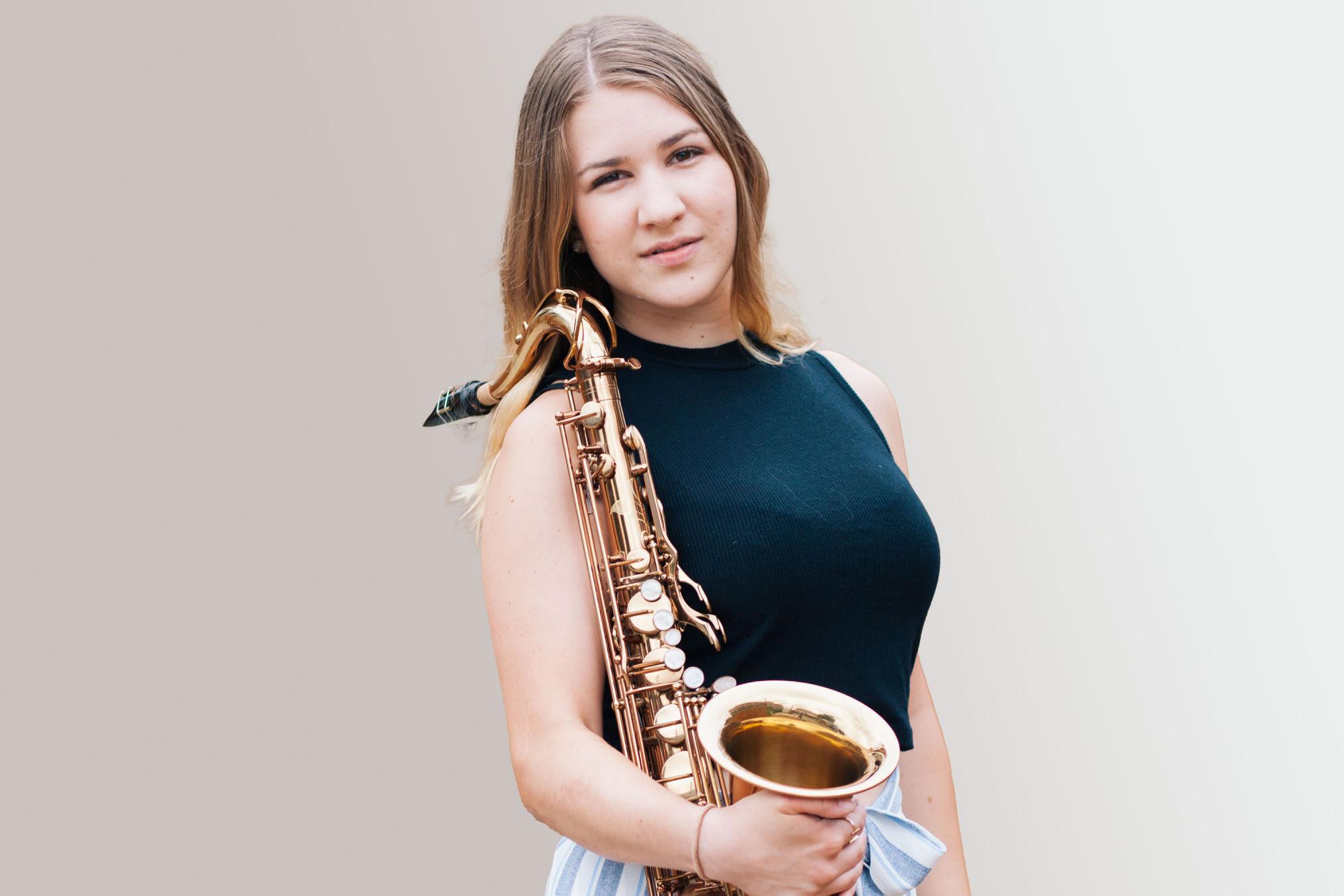 A Saxophone Student with her instrument looks into camera