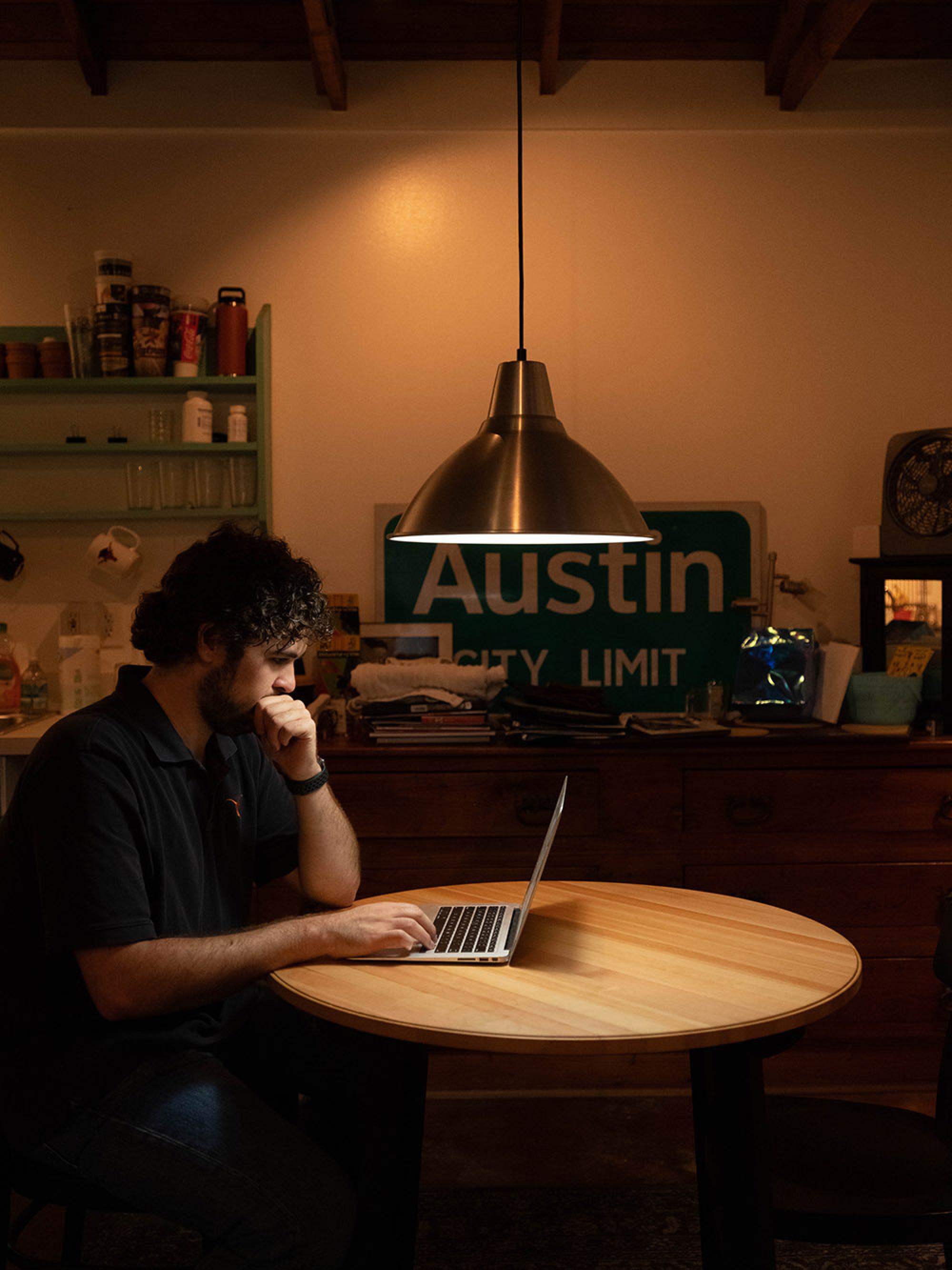 Nick sits at a daily lit table in his apartment kitchen, working on his laptop.