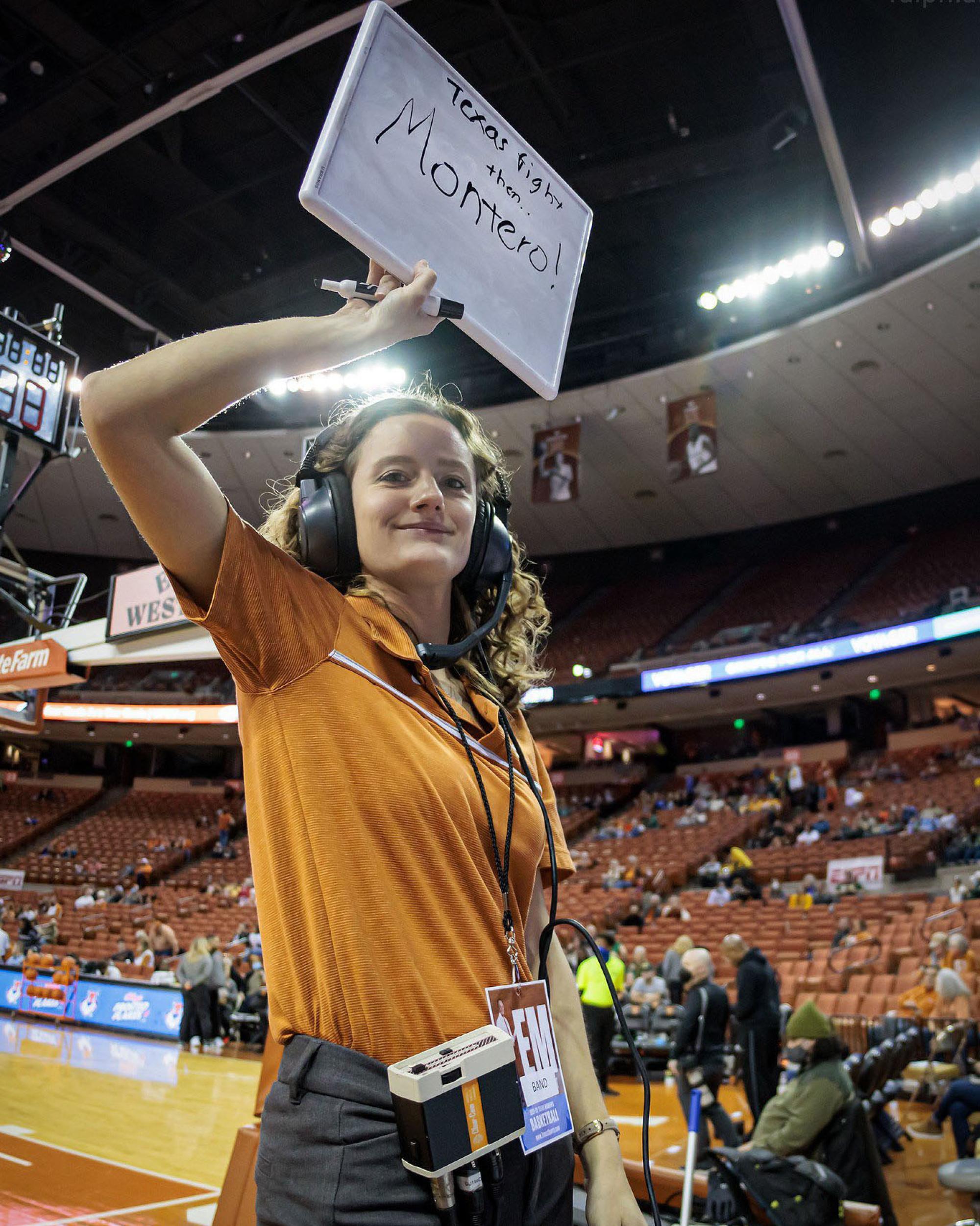 A Pep Band TA stands in front of the Band inside the stadium, holding a small white board that reads "Fight Song"