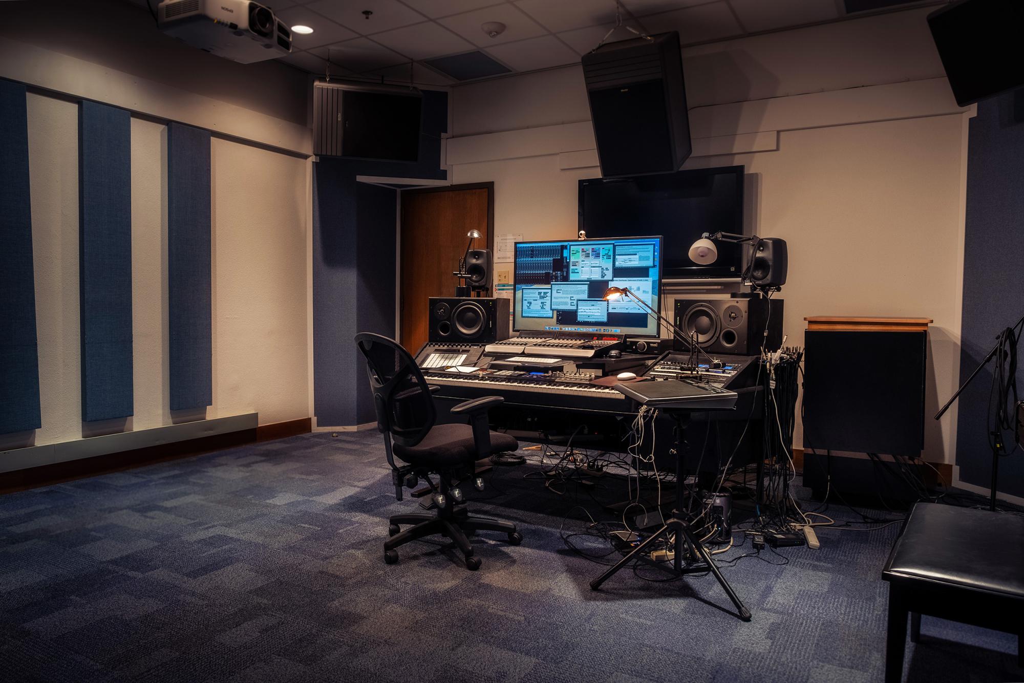 A studio mixing desk with lots of electronic music equipment in studio lined with acoustic tiling