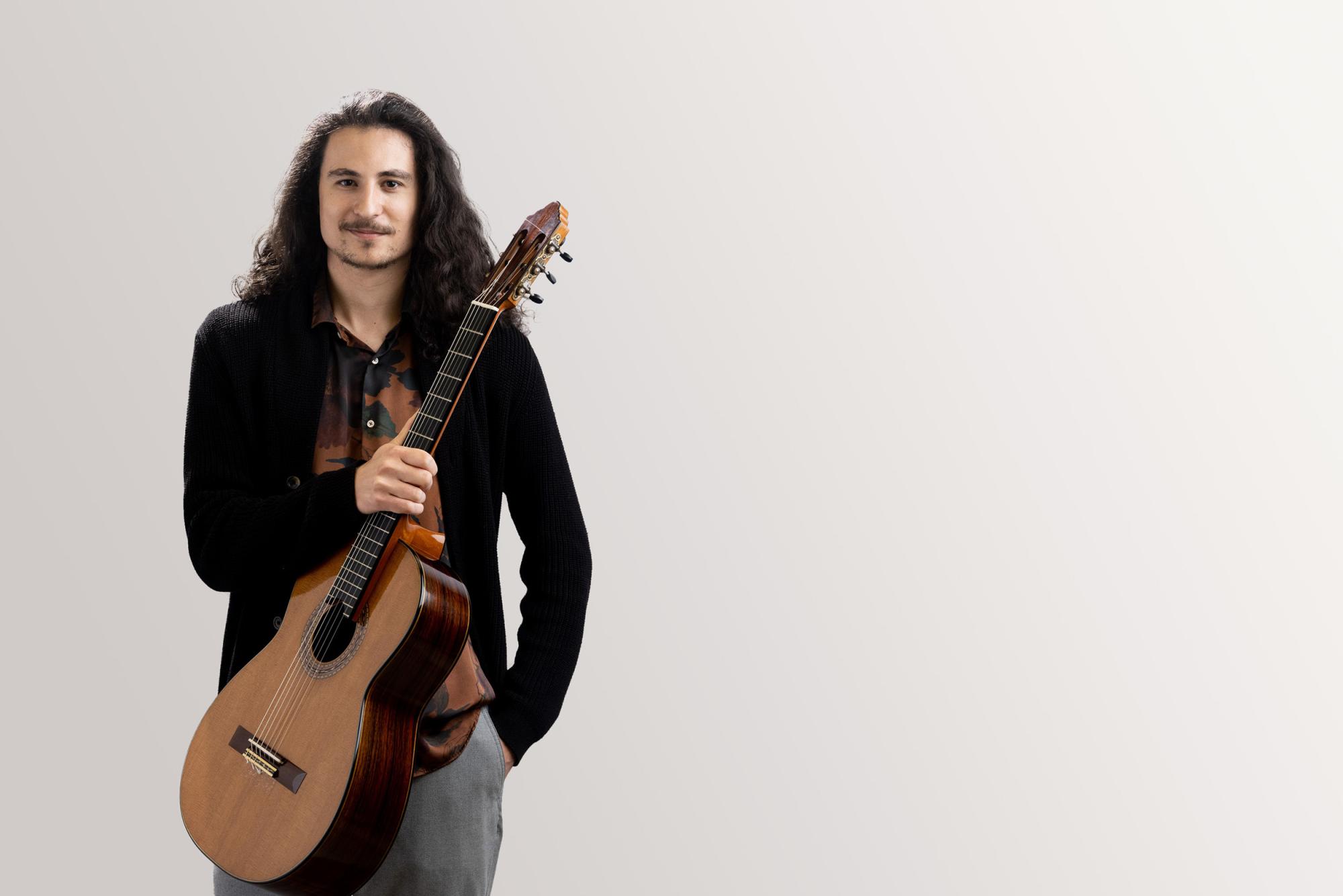 A guitar student holds his guitar while looking confidently into camera