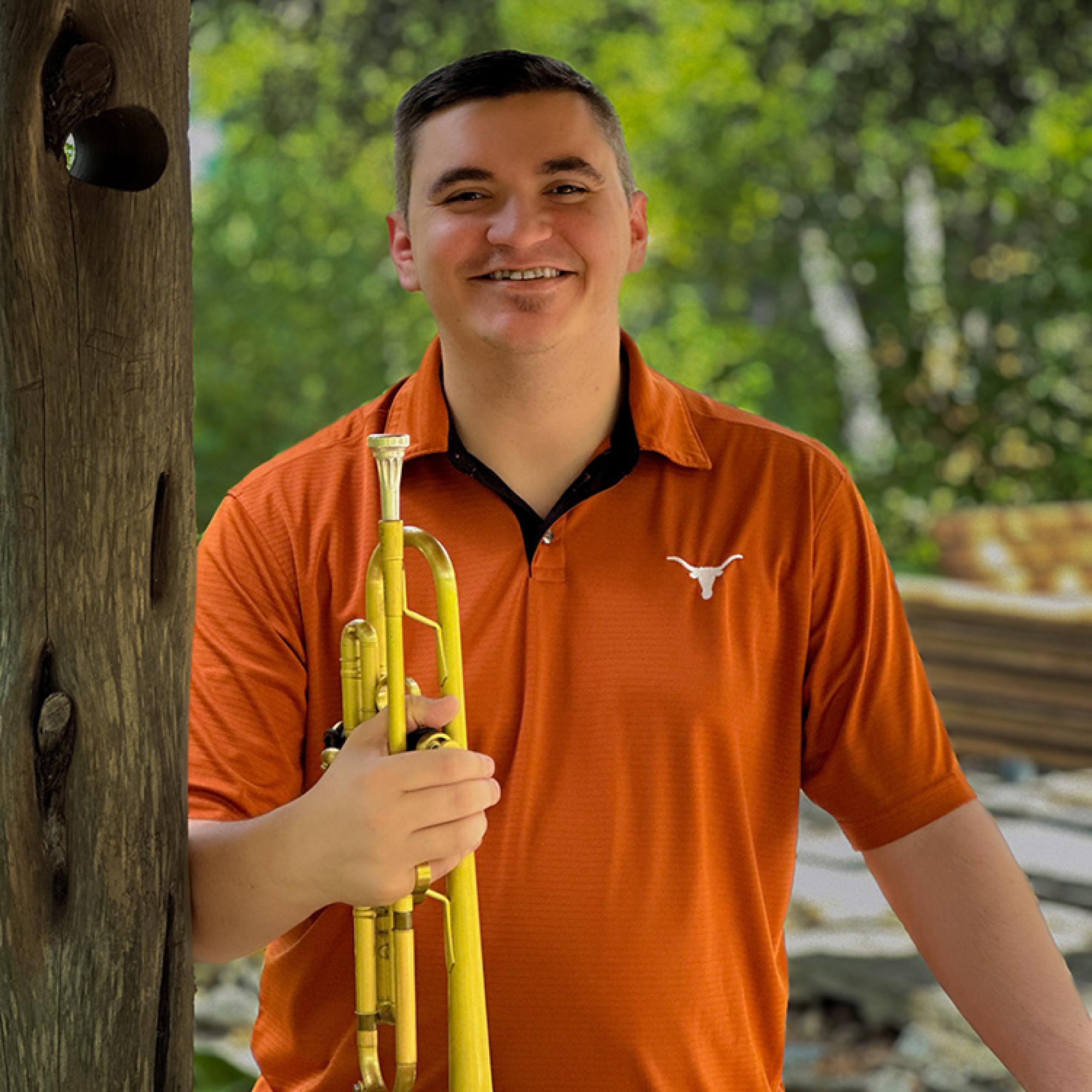 Chris Cermak, dressed in a University of Texas burnt orange short, holds his trumpet and smiles into camera.