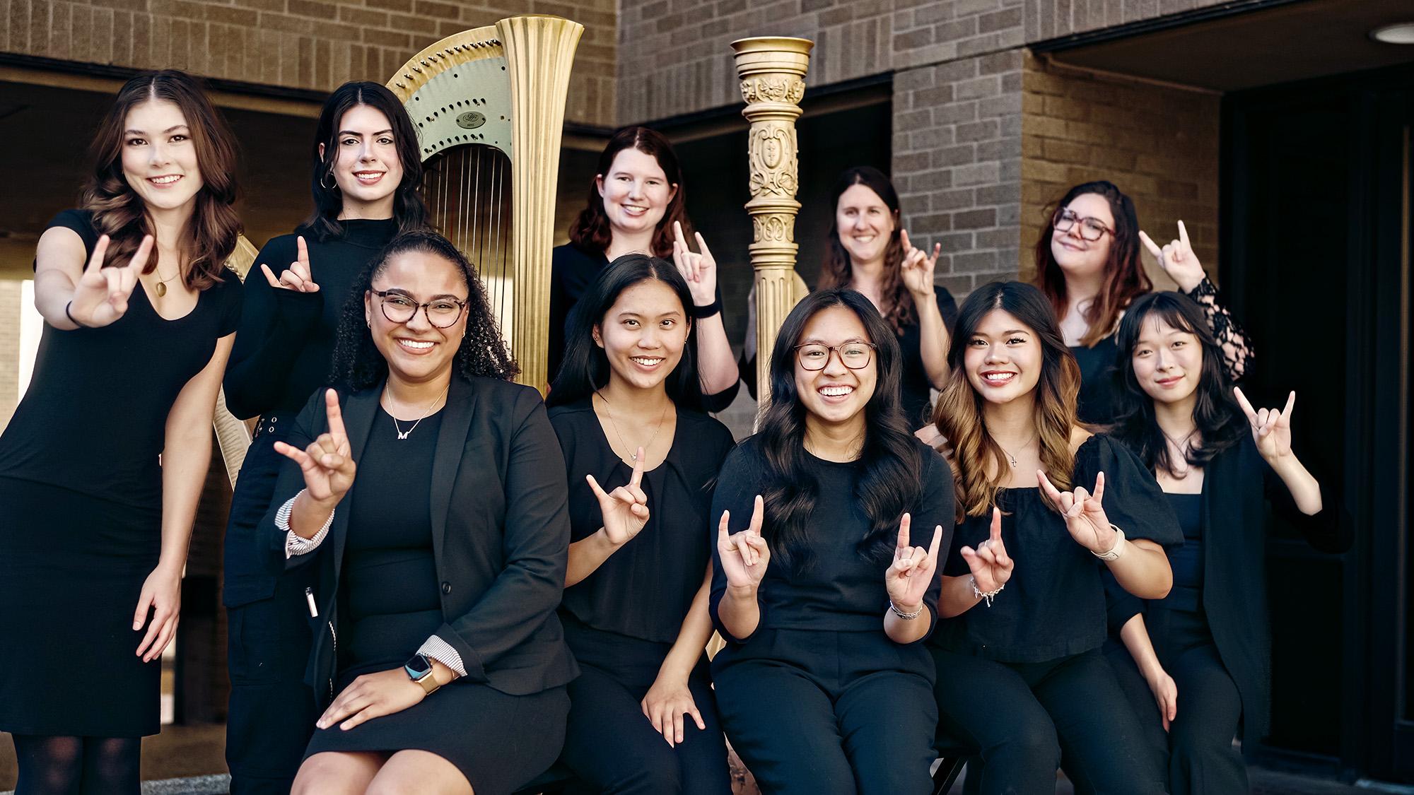 UT Harp Ensemble gather around a couple harps and raise the Hook 'em sign.