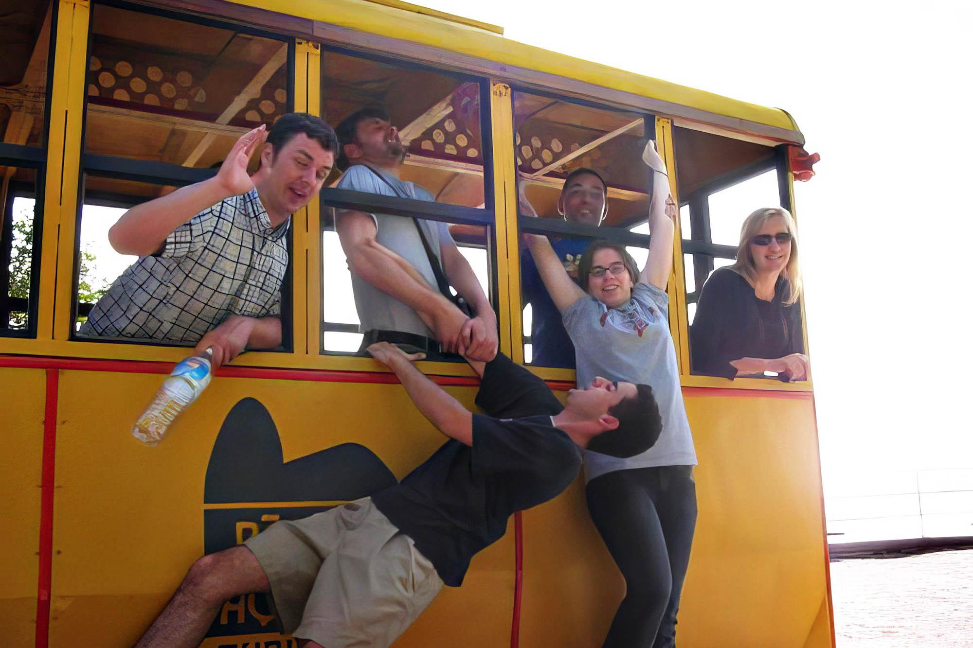 Students hang off the side of a trolly car, making silly faces for the camera