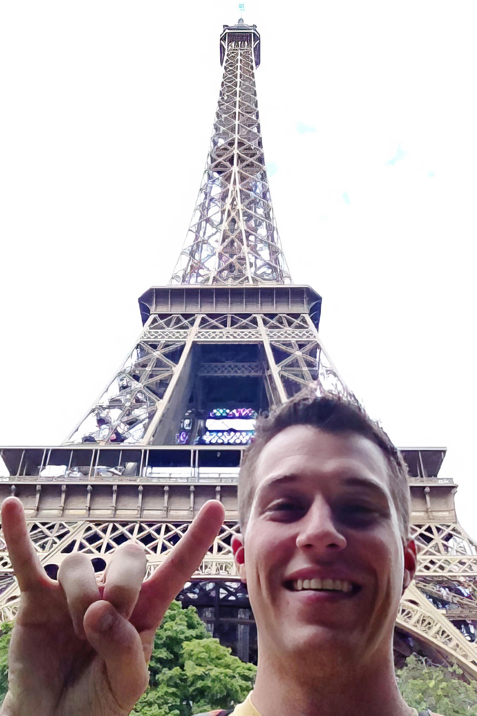 a student makes ut horns with his hand in front of the Eiffel Tower