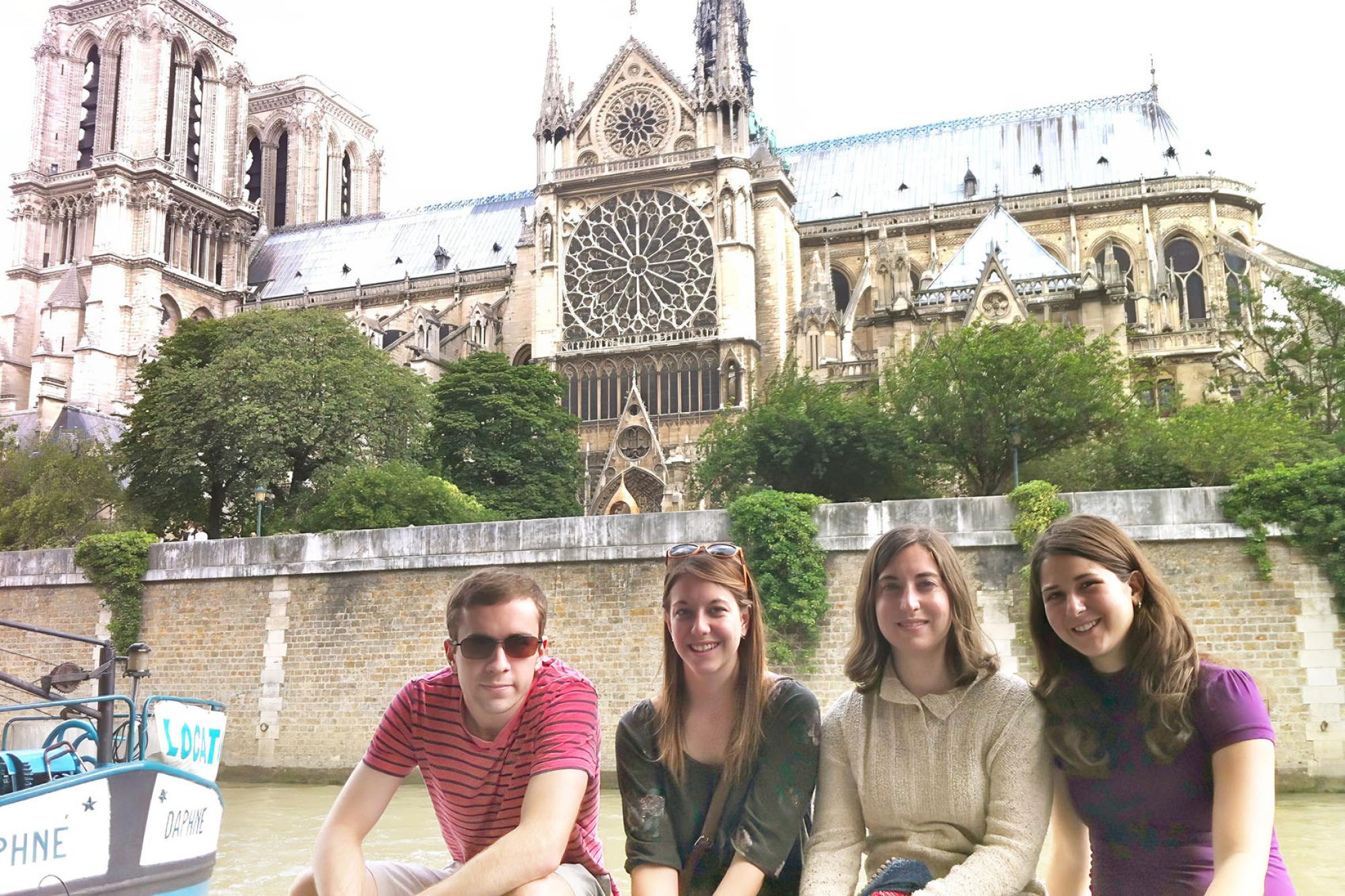 4 students sit along the banks of the Seine river, Notre Dame Cathedral is in the background