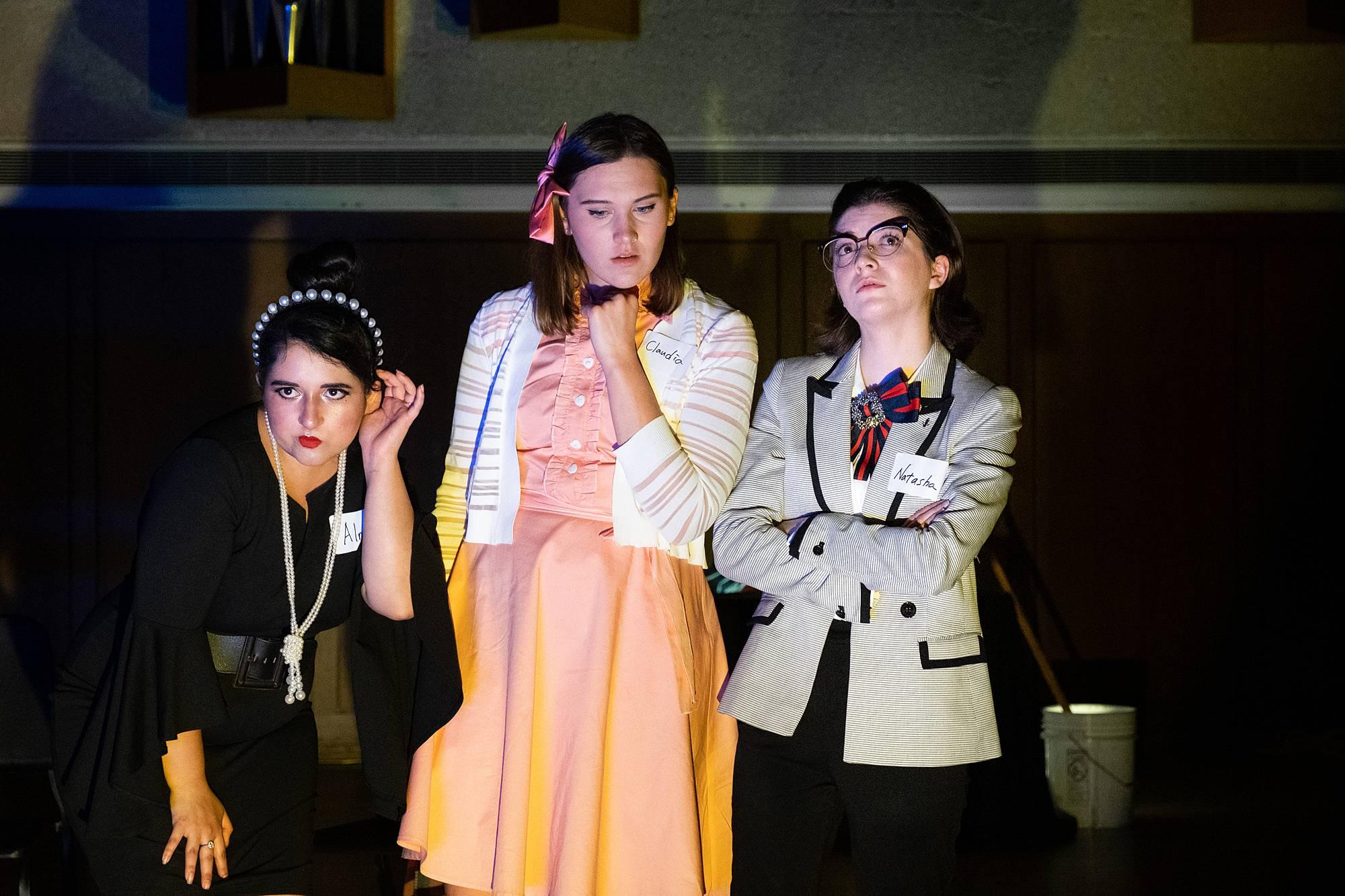 three singers stand on a darkly lit stage with somber faces of concentration