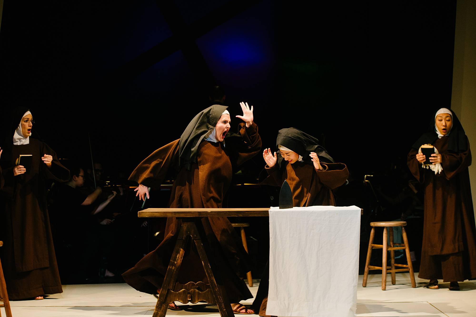 An angry nun raises her hand to strike another nun who is cowering beside her.