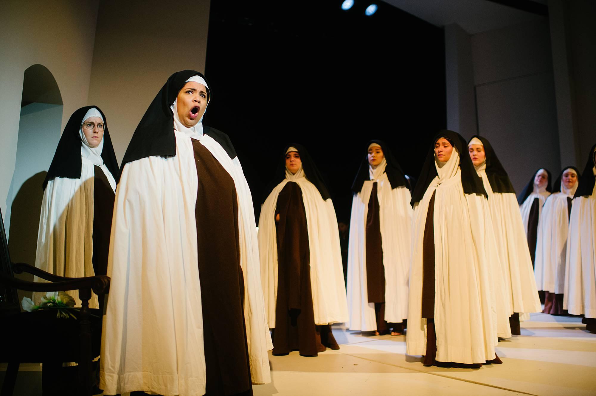 Nuns take over the stage, wearing white cloaks over their usual brown robes, the woman in the foreground sings an arial