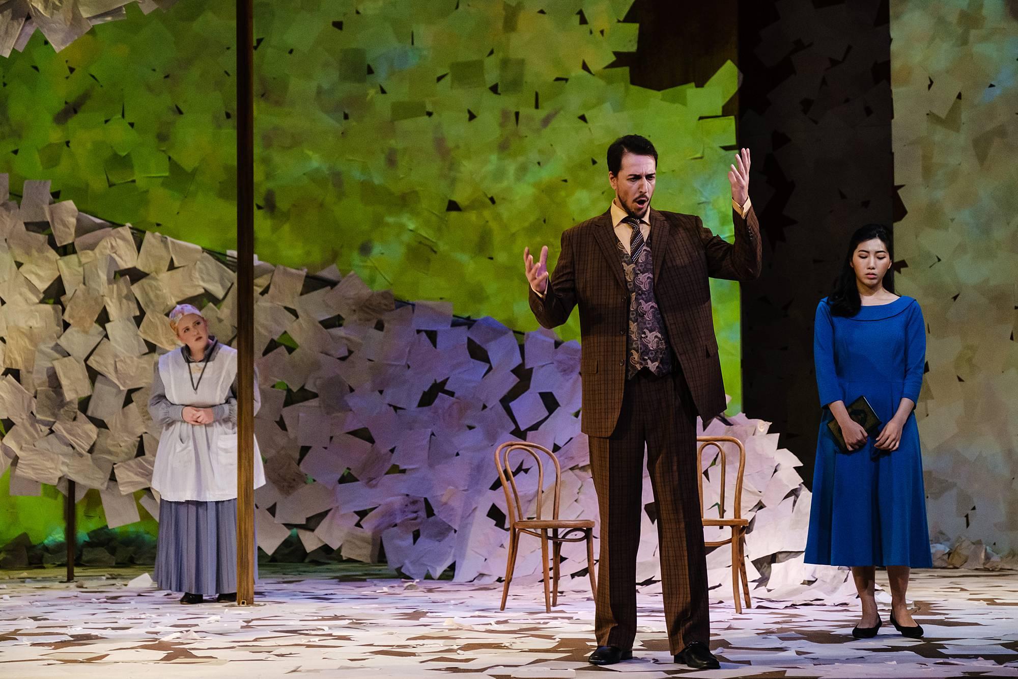 A man stands center stage sining in a fury while two women look in looking afraid and concerned.