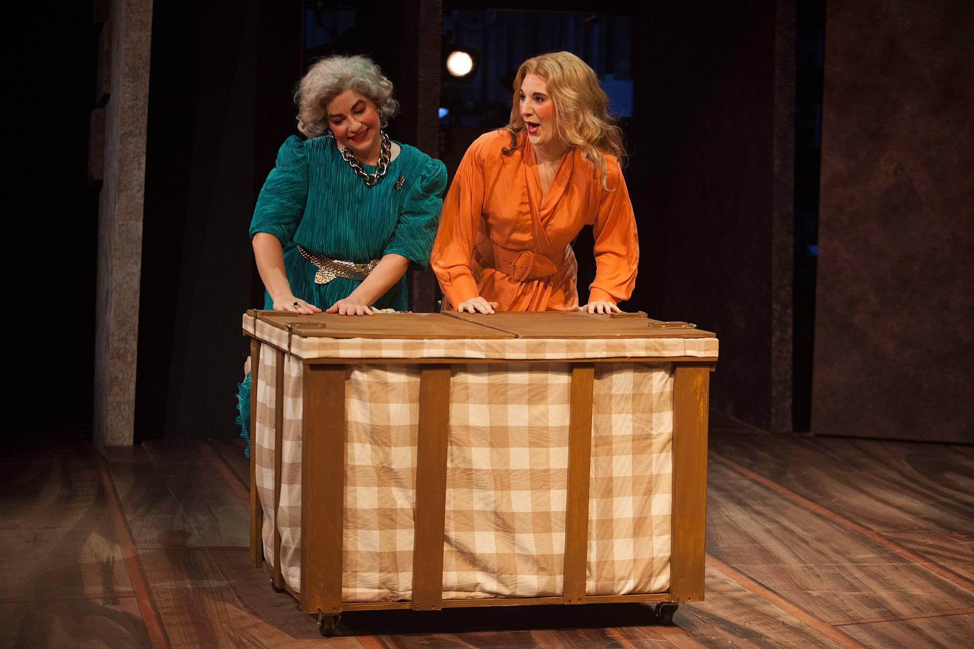 Two women push a large laundry basket onto the stage.