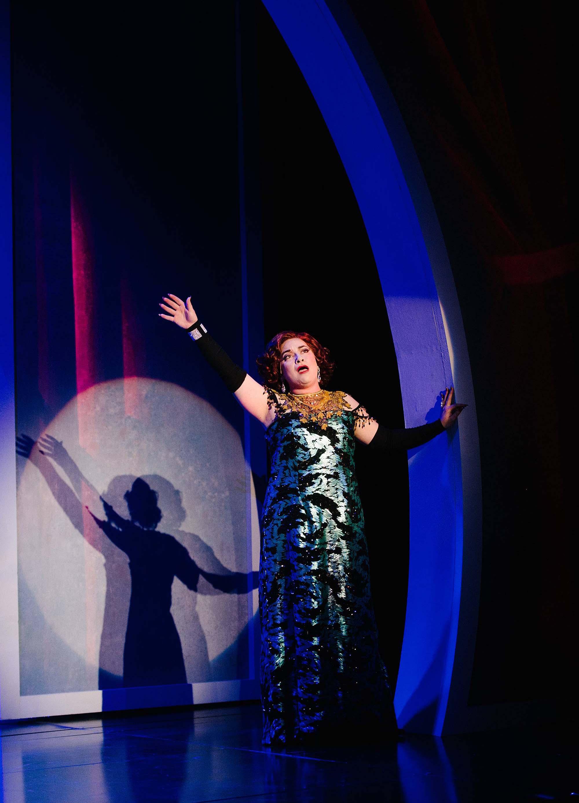 A woman in. along sequence gown and gloves performs a vaudeville number on stage.