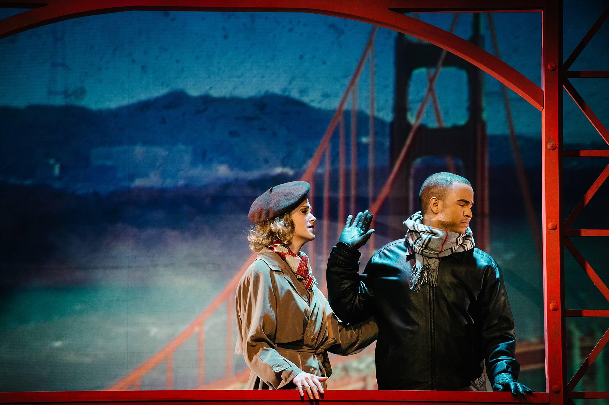 a Man and woman on the Golden Gate Bridge, the man shakes his head and holds his hand out at the woman, as if he rejects what she's saying to him.