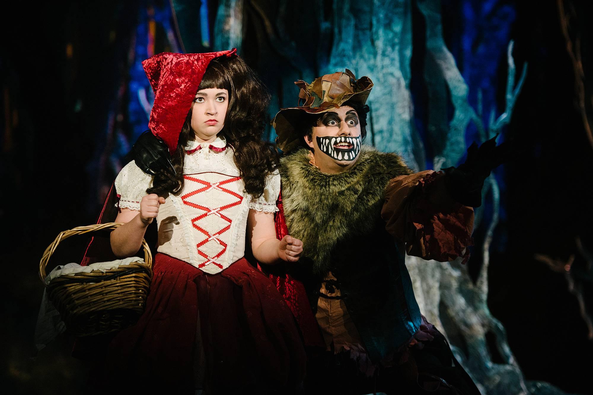 Two performers stand on a wooded set, one dressed as Little Red Riding Hood, the other is the Big Bad Wolf.