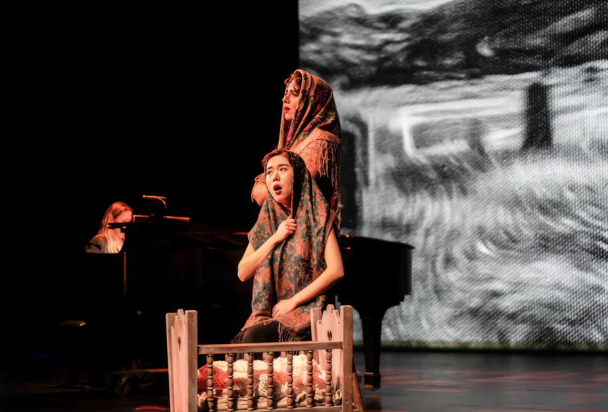 Two women with their heads covered by shawls perform on stage.