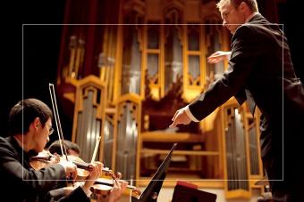 A conductor conducts a violin section in Bates Recital Hall