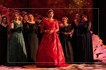 A singer in a red dress is surrounded by other singers on stage