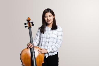 a female cellist holds her instrument and smiles