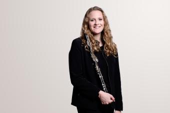 an oboist holds her instrument and smiles at the camera.