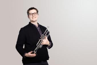 A trumpet player holds her trumpet and smiles