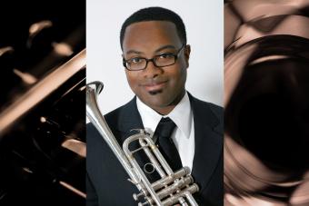 A black man wearing glasses holds a trumpet. 