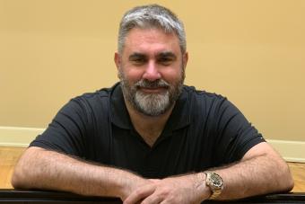 A bearded man wearing a black t-shirt smiles.