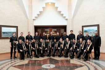 An image of the Trombone Choir holding their instruments in an elaborate hall