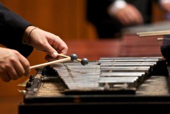 A closeup photo someone's hands playing a xylophone with wooden mallets.