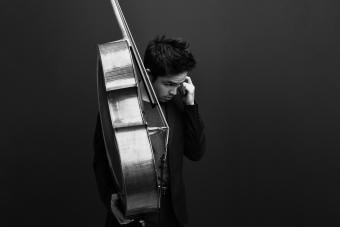 Jay Campbell holds his cello in one hand, looking introspectively away from camera