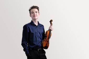 a student violinist holds his violin and looks into camera