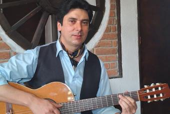 Ricardo Parra sits, holding his guitar in front of a brick wall