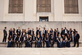 A large group of students dressed in formal attire posed casually in front of a University of Texas building. 