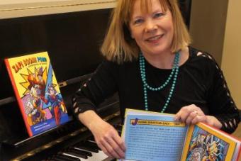 Lucy Amen Warner holds a copy of her children's book while sitting at a piano