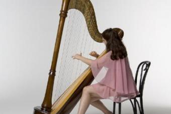 Mia Theodoratus wears a pink dress and plays the harp