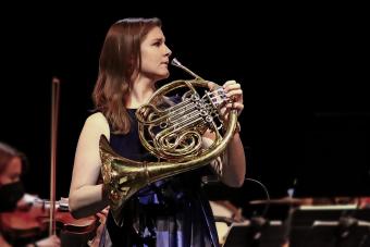 Horn player Nikolette LaBonte playing as a soloist wearing a purple dress.