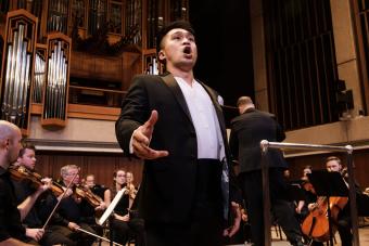 A singer in formal dress performs in front of a live orchestra